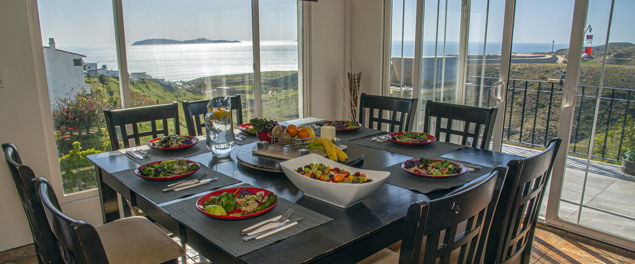 The communal dining table at The Mission Within, with an ocean view through floor-to-ceiling windows